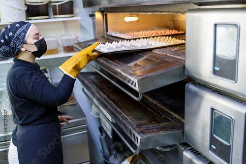 Female baker taking out tray from oven at commercial kitchen