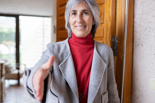 Smiling mature woman offering handshake at doorway photo