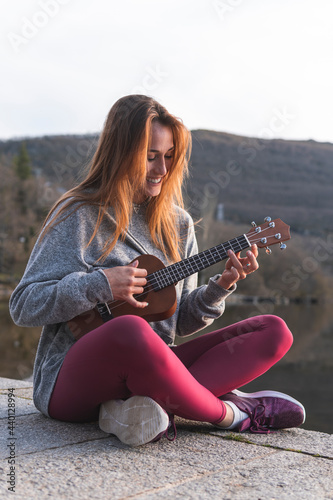 Beautiful woman playing ukulele on while sitting on promenade photo