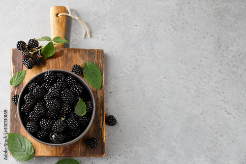 Ripe blackberries with leaves in bowl on gray background photo