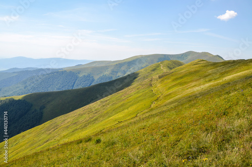 Carpathian summer landscape. Hiking path through grass field and mountain ridge with blue sky background. Ukraine