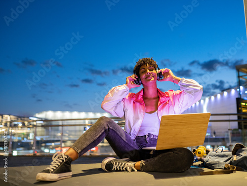 Smiling woman enjoying music on headphones while sitting outdoors at night