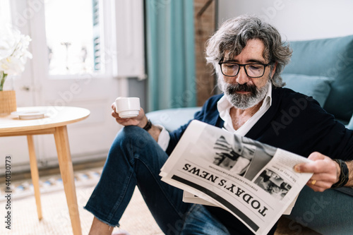 Handsome man reading newspaper holding coffee cup while sitting at home