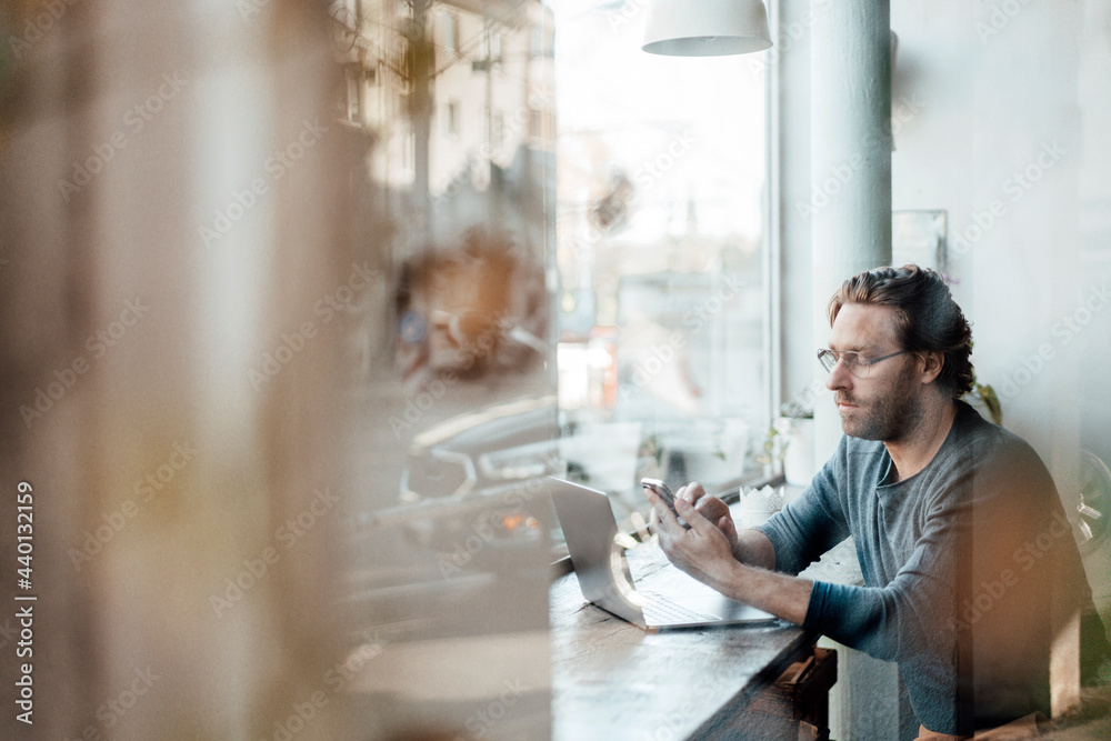 © Joseffson/Westend61 - Mature man text messaging on mobile phone by laptop at coffee shop © Joseffson/Westend61 - Mature man text messaging on mobile phone by laptop at coffee shop