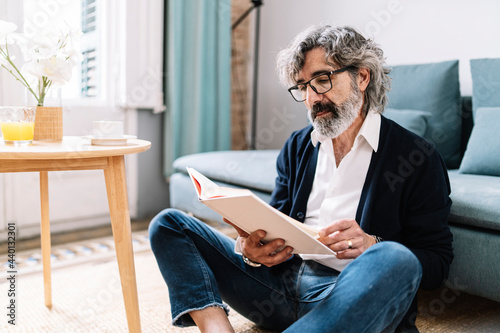Senior man reading book while sitting in living room at home