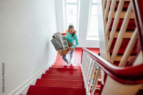 Young woman carrying cardboard boxes while moving up on staircase at home photo