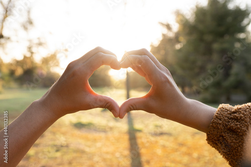 Hands of young woman making heart shape during sunset