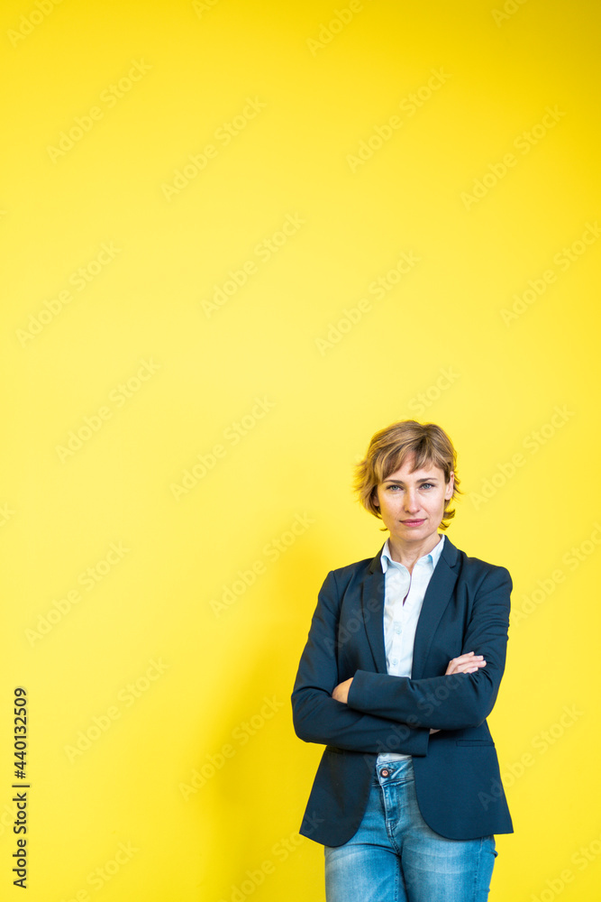 Mature female professional standing with arms crossed in front of yellow wall Mature female professional standing with arms crossed in front of yellow wall