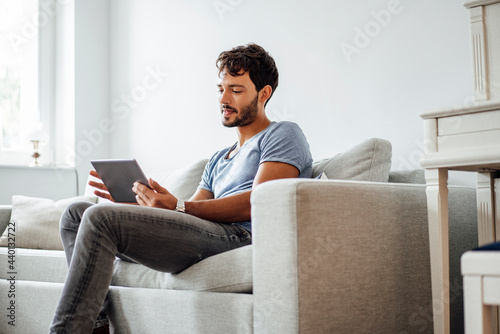 Young man using digital tablet while sitting on sofa in living room photo