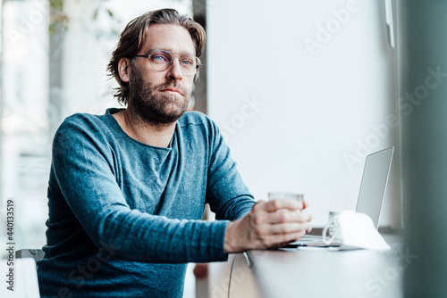 Thoughtful man by laptop in coffee shop during pandemic