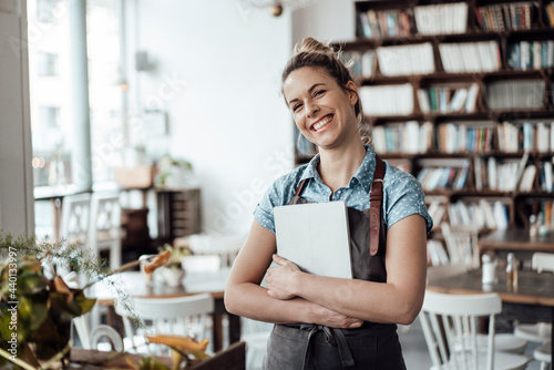 Cheerful mid adult waitress holding digital tablet at cafe photo