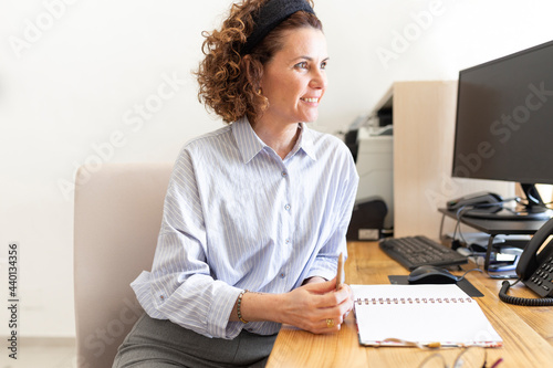 Smiling receptionist looking away while sitting at desk at hotel reception photo