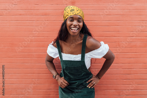 Cheerful woman with hand on hip by wall