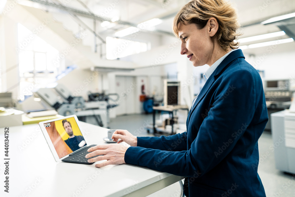 Mature businesswoman looking at colleague on video call through digital tablet in workshop Mature businesswoman looking at colleague on video call through digital tablet in workshop