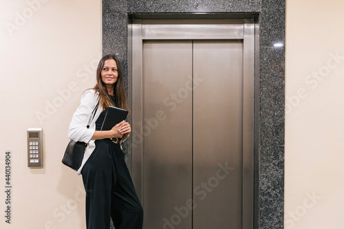 Female entrepreneur holding book while standing by elevator photo