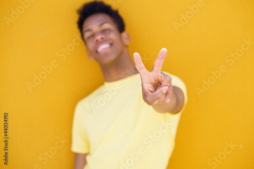 Smiling man showing peace gesture in front of yellow wall photo
