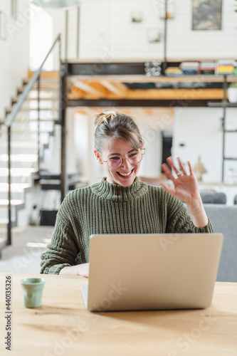 Female entrepreneur waving during video call on laptop at home photo