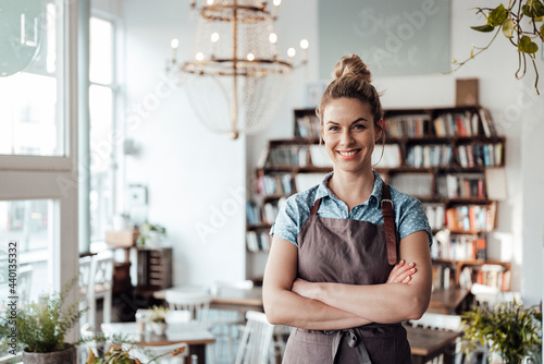 Confident mid adult waitress standing with arms crossed at coffee shop