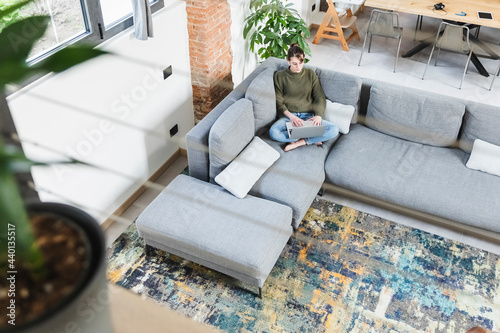 Young woman using laptop while sitting on sofa in living room at home