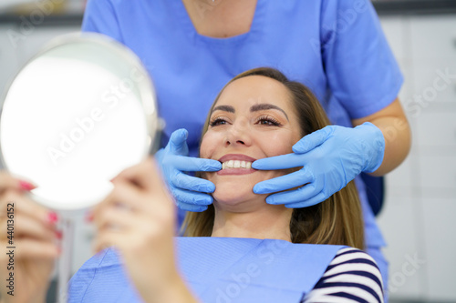 Female dentist showing teeth of patient in mirror at clinic photo