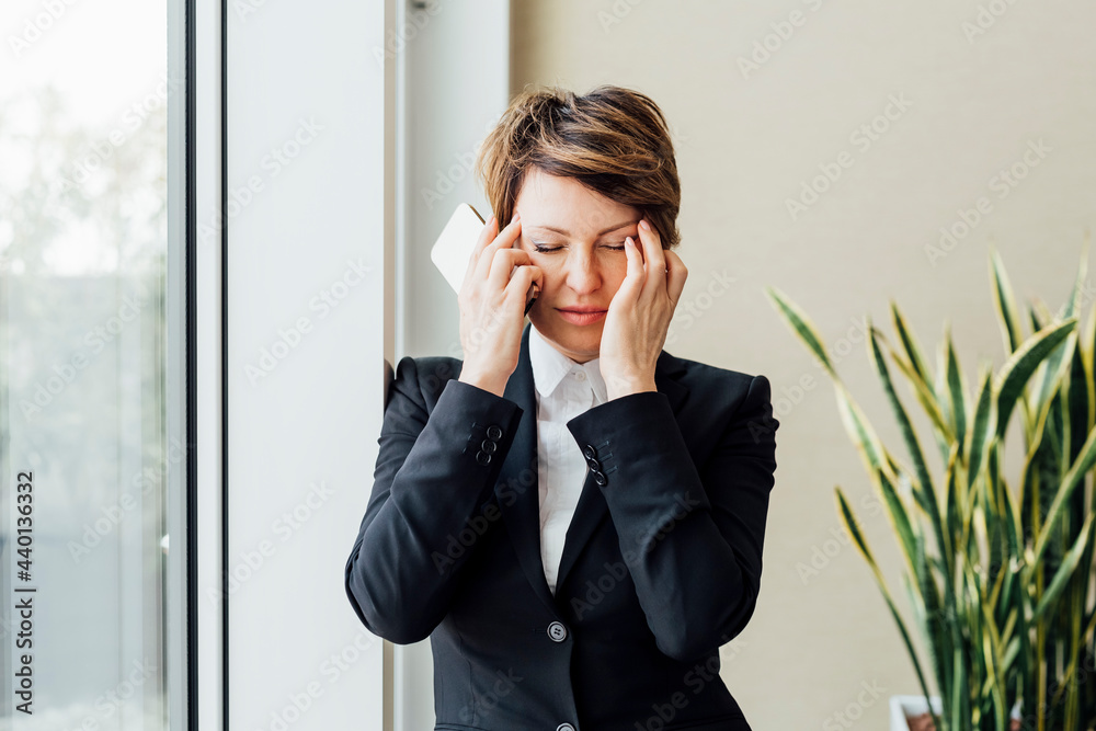 Tired businesswoman with eyes closed holding mobile phone in office Tired businesswoman with eyes closed holding mobile phone in office