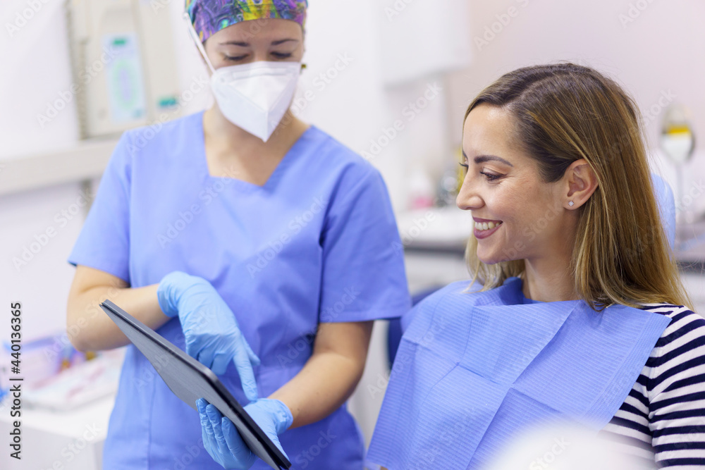 Female dentist showing digital tablet to smiling patient at clinic Female dentist showing digital tablet to smiling patient at clinic