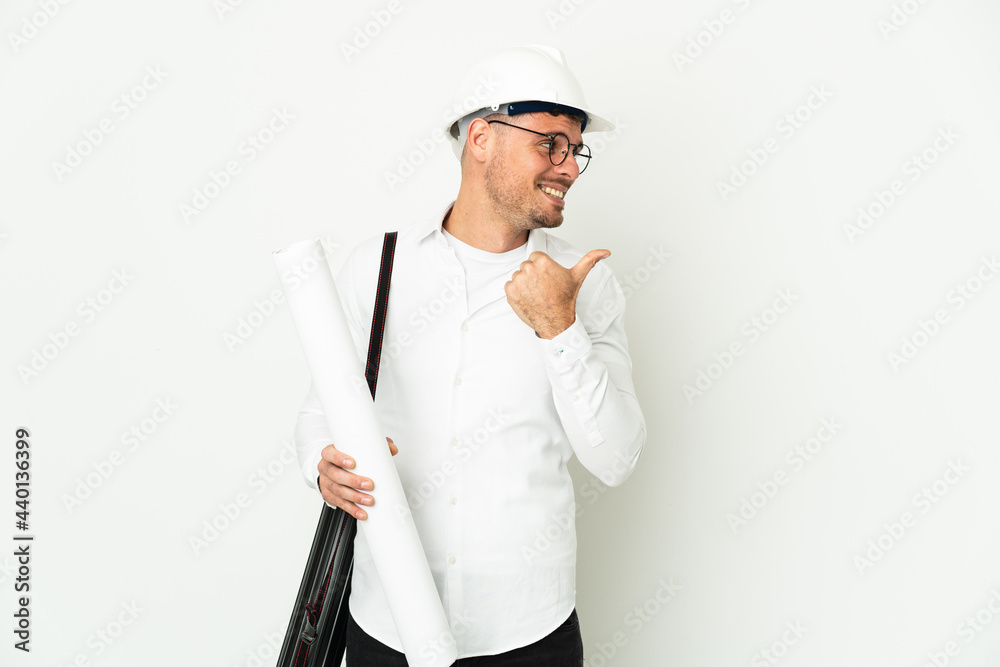 Young architect man with helmet and holding blueprints isolated on white background pointing to the side to present a product Young architect man with helmet and holding blueprints isolated on white background pointing to the side to present a product