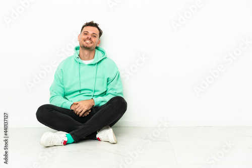 Young handsome caucasian man sitting on the floor laughing