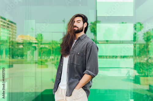 Young male hipster with long brown hair standing in front of glass wall