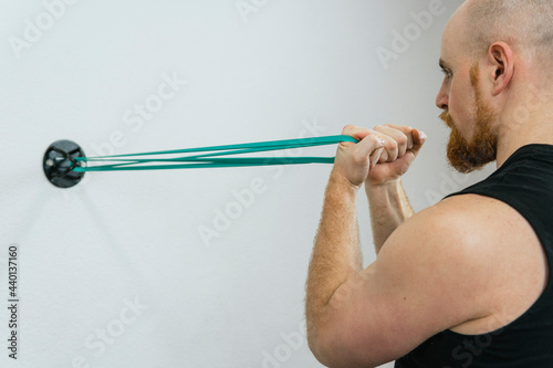 Man practicing bicep exercise through resistance band tied on wall in exercise room photo