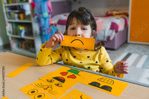 Girl holding sad face emoticon while playing at home