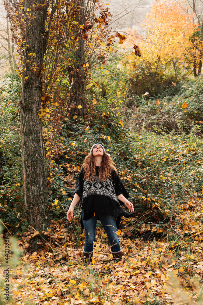 Woman looking at autumn leaves in mid-air while standing in forest during vacation Woman looking at autumn leaves in mid-air while standing in forest during vacation