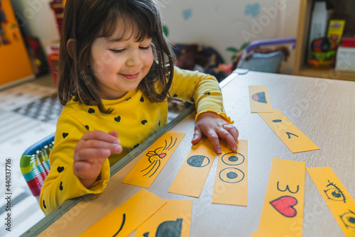 Cute girl playing with smileys on table in playroom at home