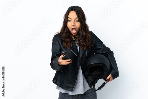 Young woman holding a motorcycle helmet over isolated white background surprised and sending a message