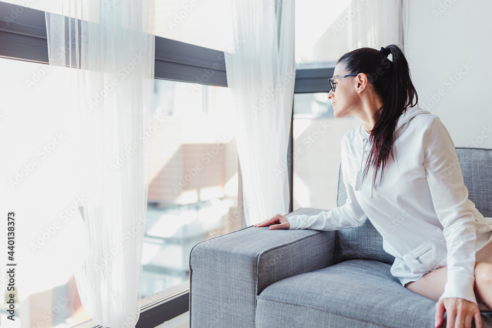 Woman sitting on sofa while looking through window at home Woman sitting on sofa while looking through window at home