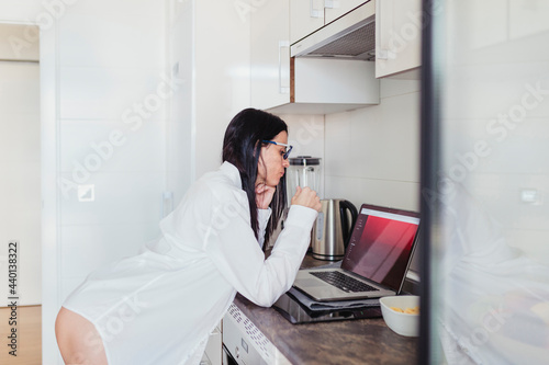 Sensual female professional using laptop in kitchen while working at home photo