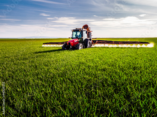 Tractor spraying pesticide on green agricultural field photo