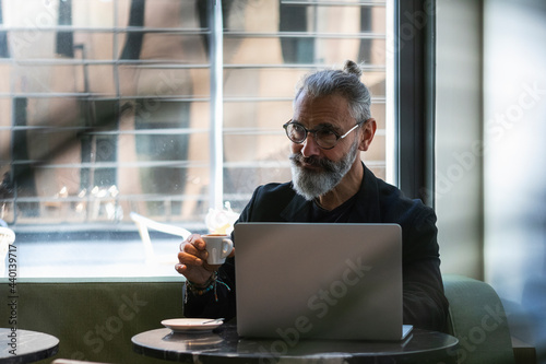 Smiling hipster male entrepreneur contemplating while having coffee cup in shop photo