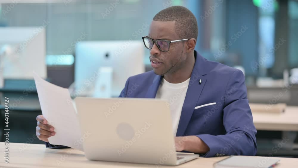 Businessman with Laptop Reading Documents in Office Businessman with Laptop Reading Documents in Office