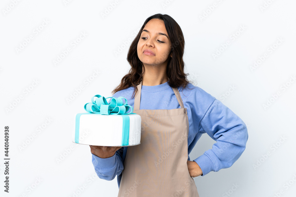 Pastry chef holding a big cake over isolated white background having doubts while looking side Pastry chef holding a big cake over isolated white background having doubts while looking side