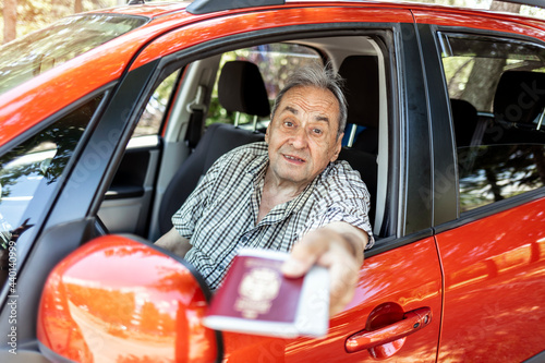 Mature man in a car showing his passport and Covid-19 vaccine record card. Traveling with vaccine passport of COVID-19. Caucasian man holding vaccine passport, sitting in the driver's seat of his car. photo