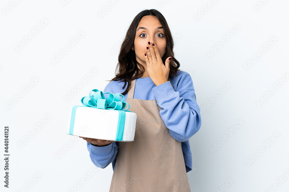 Pastry chef holding a big cake over isolated white background covering mouth with hands Pastry chef holding a big cake over isolated white background covering mouth with hands
