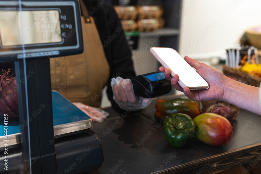 Woman holding smart phone over credit card reader while paying at grocery store Woman holding smart phone over credit card reader while paying at grocery store