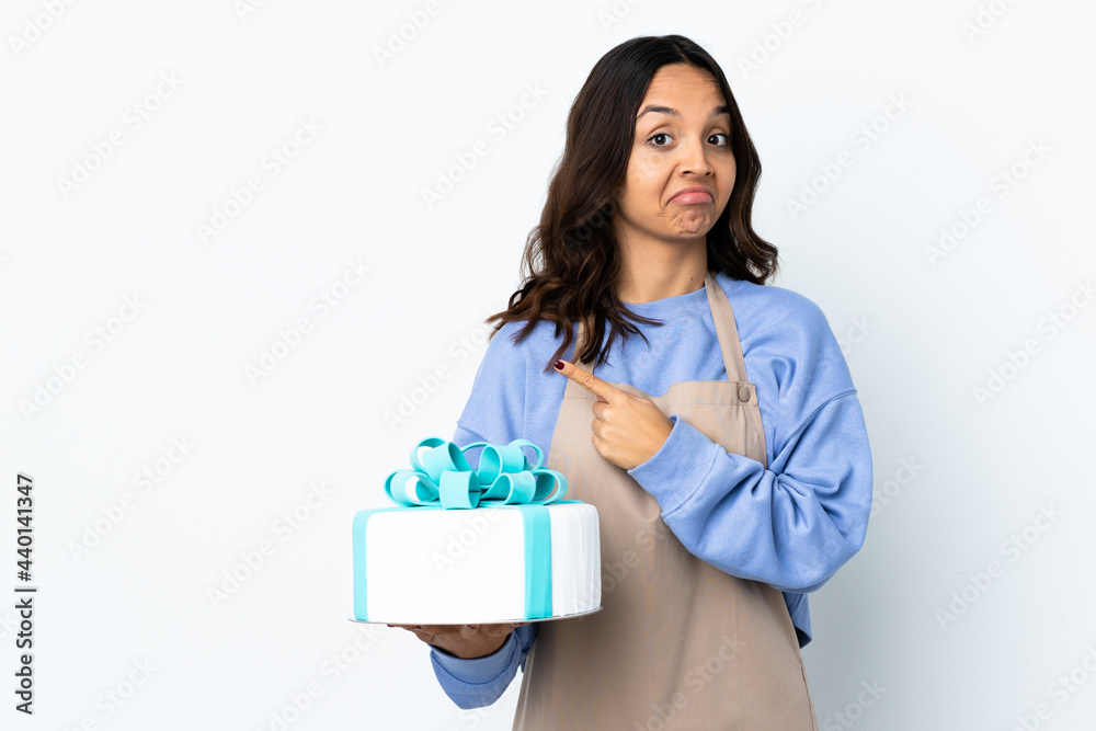Pastry chef holding a big cake over isolated white background pointing to the laterals having doubts Pastry chef holding a big cake over isolated white background pointing to the laterals having doubts