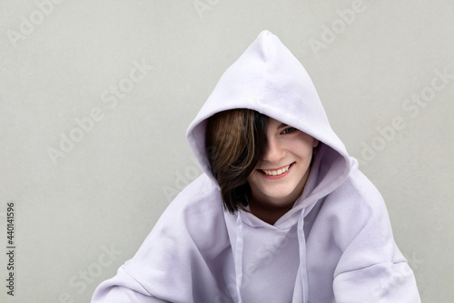 Smiling girl wearing purple hooded shirt by gray wall photo