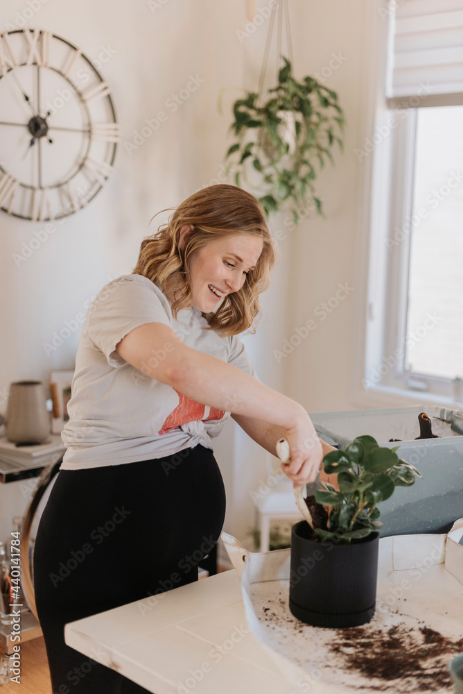 Happy woman putting soil in potted plant at home Happy woman putting soil in potted plant at home