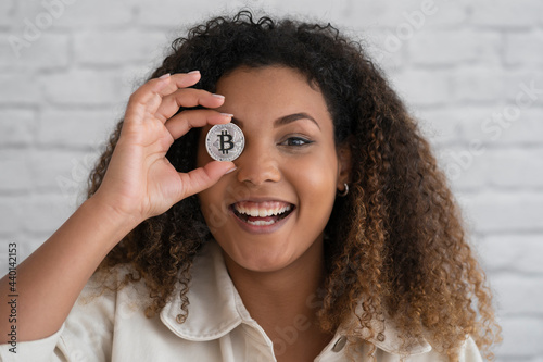 Smiling woman covering eye with silver cryptocurrency photo