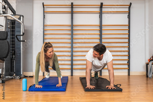 Smiling male and female athletes doing push-ups on exercise mat in gym photo