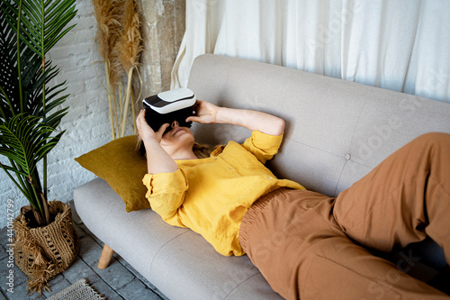 Woman using Virtual reality simulator while lying on sofa at home photo