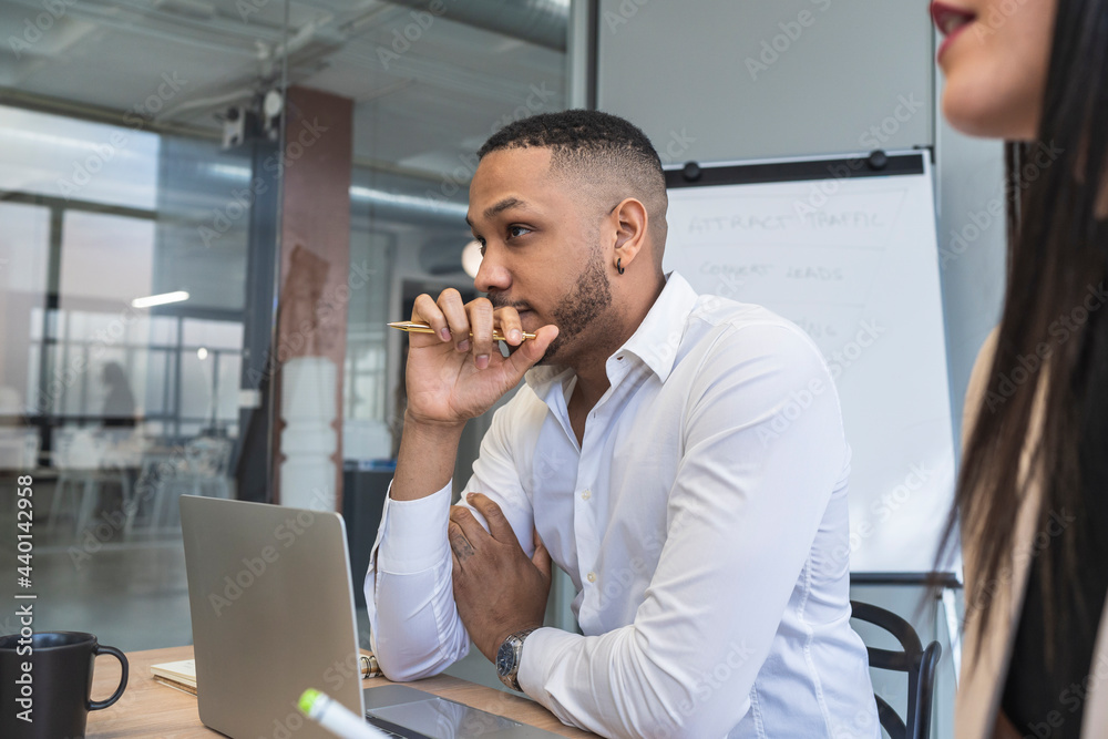 Thoughtful businessman looking away while sitting by female colleague in coworking office Thoughtful businessman looking away while sitting by female colleague in coworking office